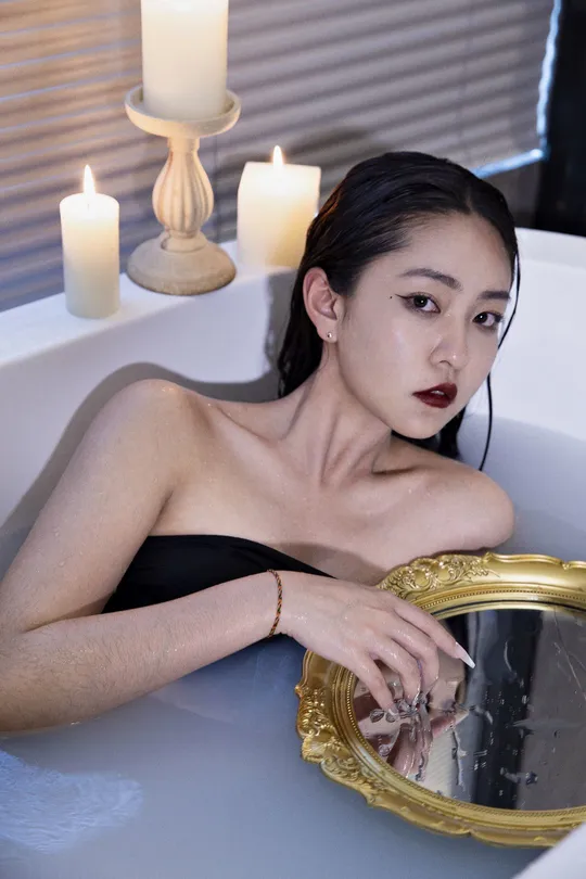 一个穿黑色衣服的女人坐在浴缸里 周围有蜡烛和镜子。
