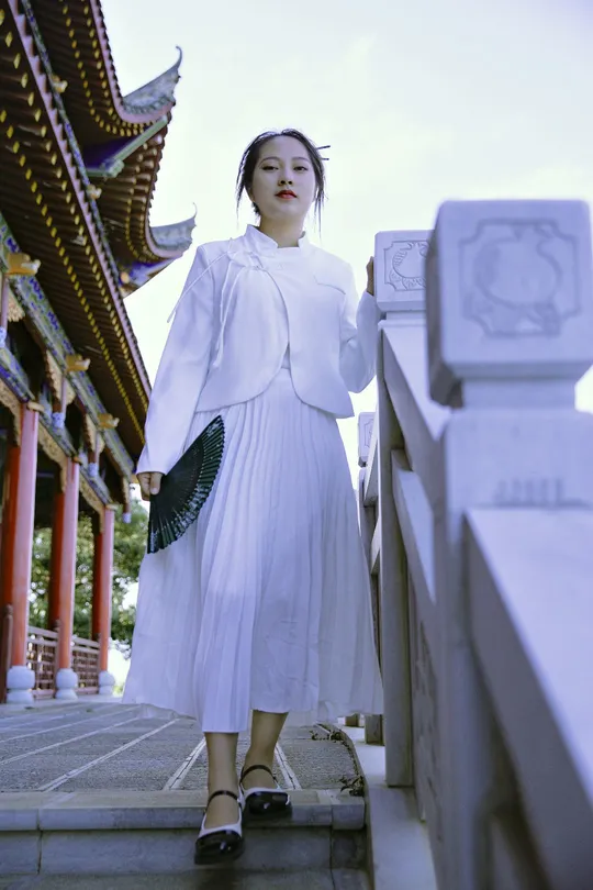 一位穿着白色连衣裙的年轻女子站在一座寺庙前的桥上