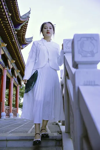 一位穿着白色连衣裙的年轻女子站在一座寺庙前的桥上