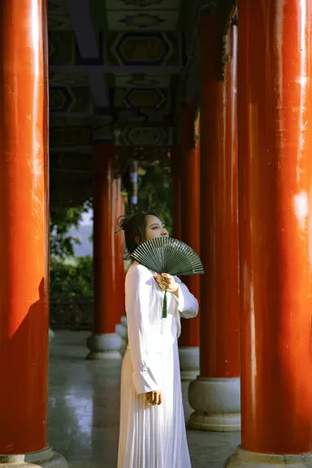 一位身着传统白色长裙 手持雨伞 站在带红柱的寺庙中的女士。