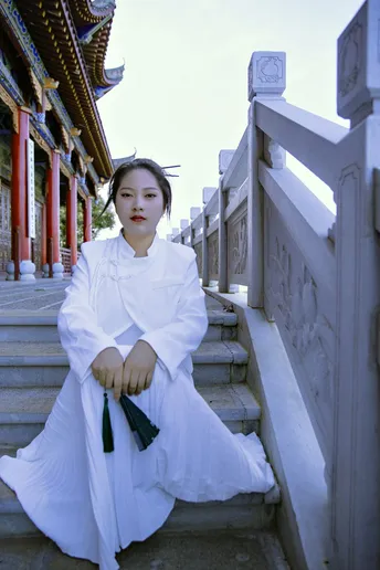 一位身着传统白色长裙的年轻女子坐在寺庙的台阶上
