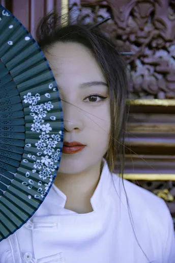 一位年轻女士穿着一件白色雨伞 举着一把扇子遮在她脸上。