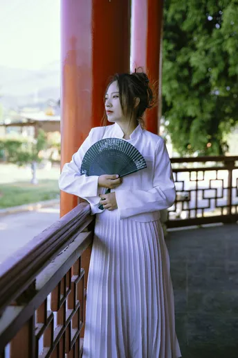 一位穿着白色和服的年轻女子在寺庙拿着扇子