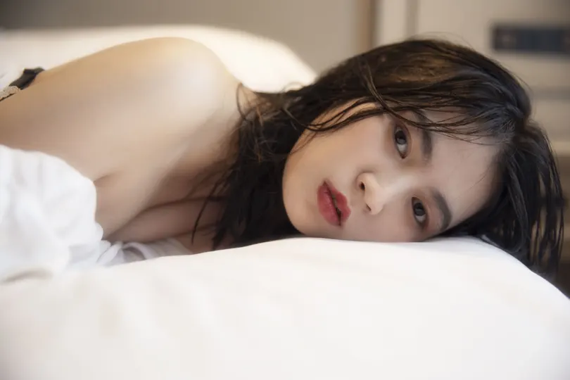 一个年轻女子躺在带有白色床单和枕头的床上