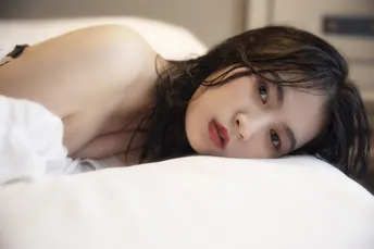 一个年轻女子躺在带有白色床单和枕头的床上