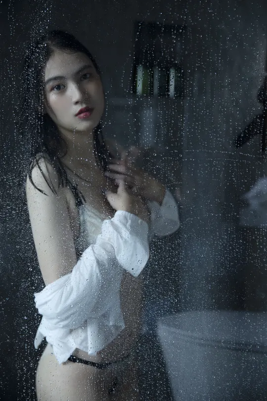 一位孕妇站在淋浴间里 浴室里有一扇湿漉漉的玻璃窗。