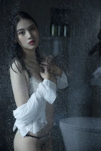 一位孕妇站在淋浴间里 浴室里有一扇湿漉漉的玻璃窗。