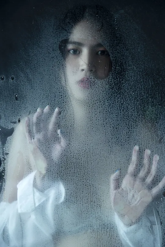 一位女士用双手按在窗户玻璃上 正在透过窗户看