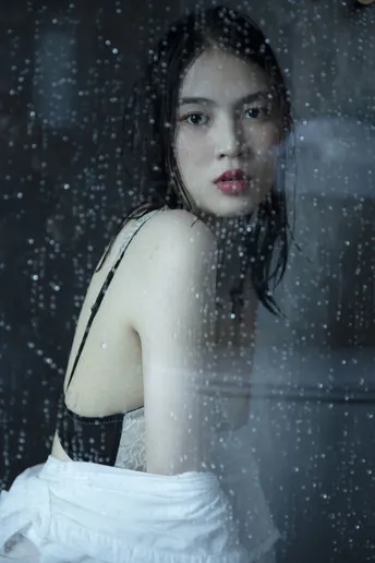 一位穿着白色连衣裙的年轻女子 带着一把雨伞 凝视着一扇湿漉漉的窗户。