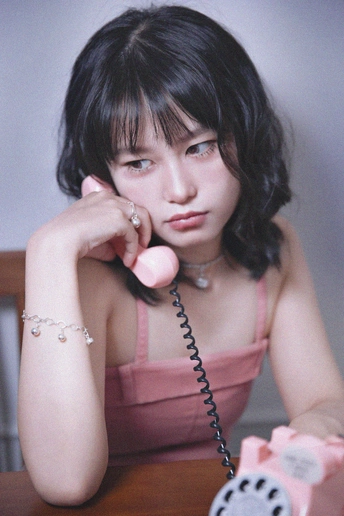 一个穿着粉红色连衣裙的年轻女子坐在桌子旁打电话