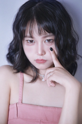 一位年轻女子穿着粉色裙子 手指上戴着戒指 举起手来挡住自己的脸。