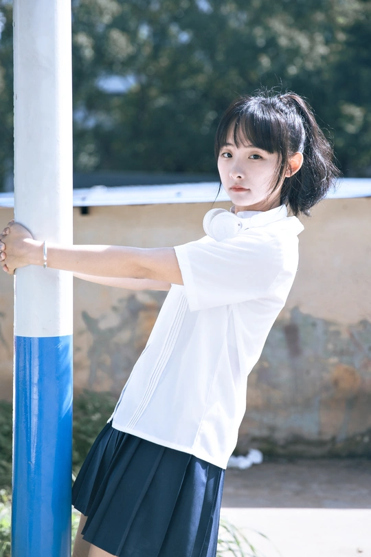 一位穿着白衬衫和蓝色裙子的年轻女子抓住一根杆子