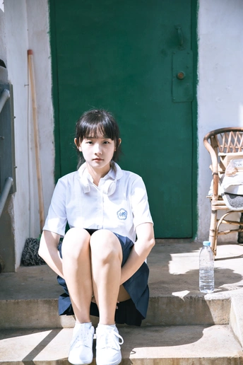 一个穿制服的年轻女孩坐在一些台阶上 位于一所房子的门前。