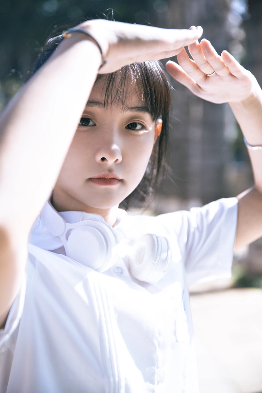 一位年轻女子举起双手捂住眼睛 凝视着相机。