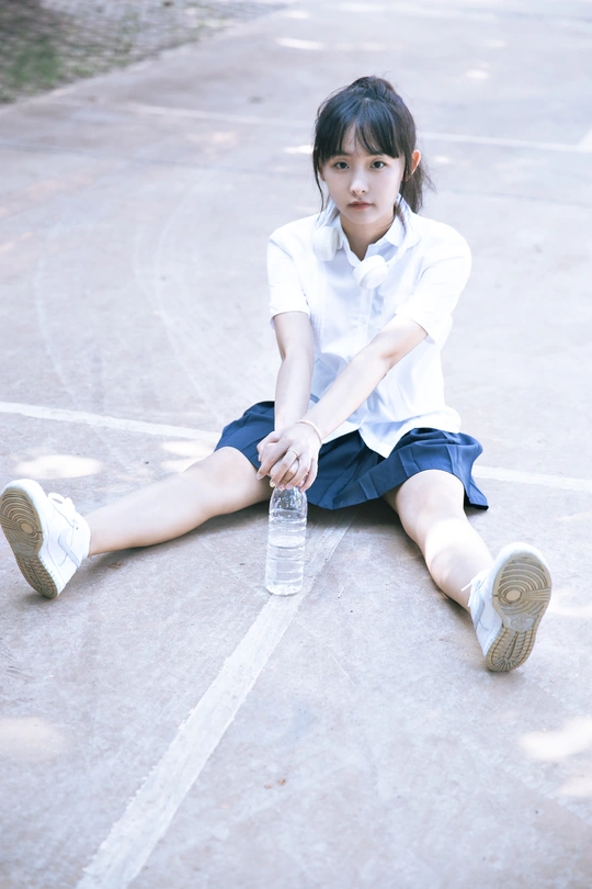 一个小女孩穿着制服坐在地板上 手里拿着一瓶水。