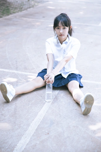 一个小女孩穿着制服坐在地板上 手里拿着一瓶水。