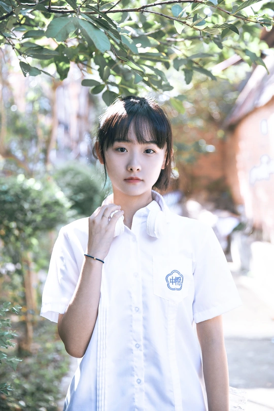 一个穿着白衬衫的年轻女孩站在一棵树下