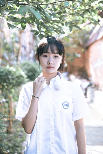 一个穿着白衬衫的年轻女孩站在一棵树下