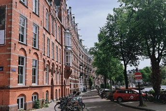 一条街道 有高大的砖楼 汽车和自行车停在人行道上。