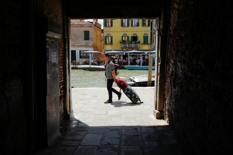 一条狭窄的巷子 一个人推着一个箱子 另一个人提着一个箱子走下建筑物之间的隧道。