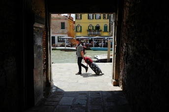 一条狭窄的巷子 一个人推着一个箱子 另一个人提着一个箱子走下建筑物之间的隧道。