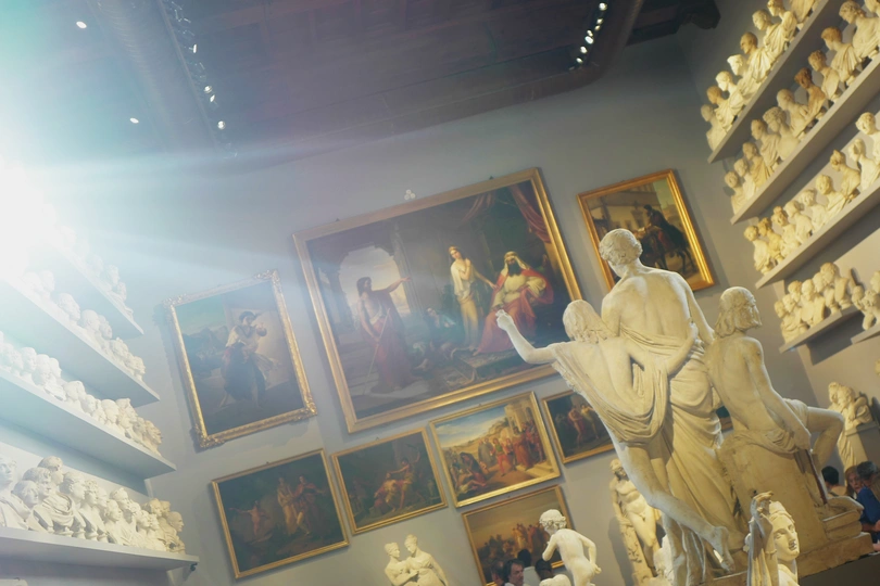 一个房间 墙上挂满了画作和图片 中央摆放着一座雕像和花瓶。