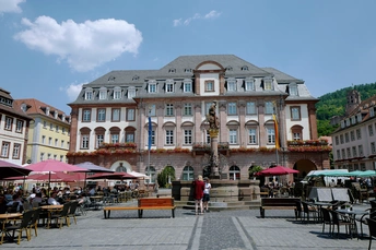 许多人坐在城市的一个大广场上 桌子上有遮阳伞。