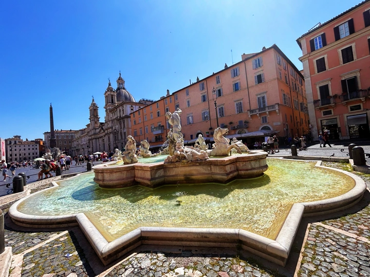 一个有喷泉的广场 背景中有人和建筑物。