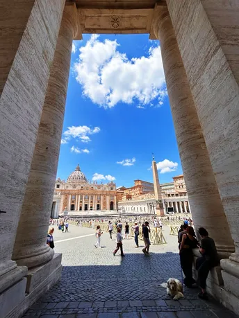 一个带柱子的庭院 人们走动 前景是一只狗 背景是天空。