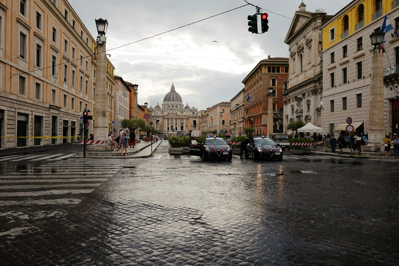 一条湿漉漉的街道 有汽车、人、建筑和交通信号灯。