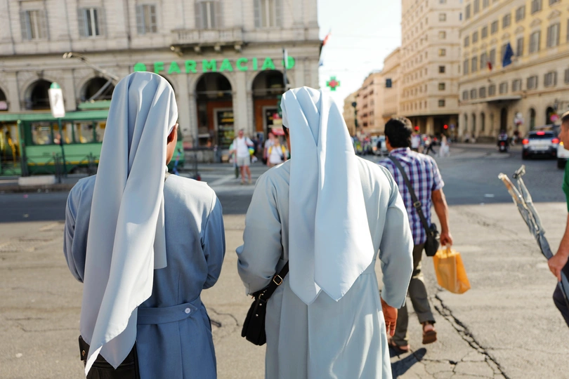 一个人穿着修女装在城市街道上行走 其他人在人行道上行走。