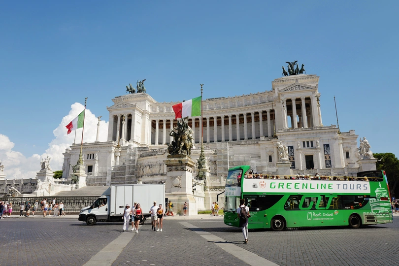 一辆绿色公交车驶过一座大型白色建筑前 该建筑前有一尊雕像。