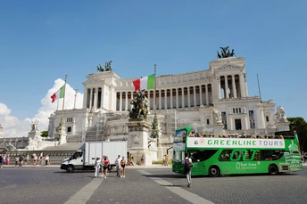 一辆绿色公交车驶过一座大型白色建筑前 该建筑前有一尊雕像。