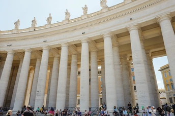 许多柱子和支柱的大型建筑站在人群前面。