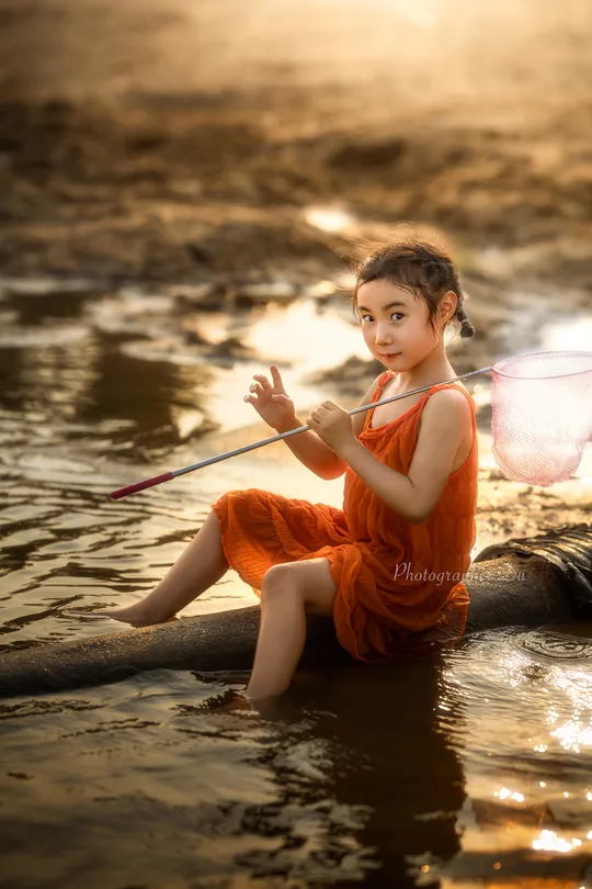 一个穿着橙色衣服的小女孩坐在小船里在河上