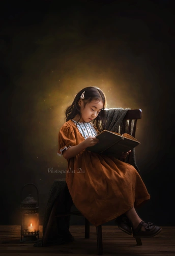 一个年轻女孩坐在一个由灯笼照亮的黑暗椅子上读书。