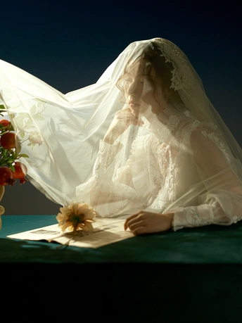 一位穿着婚纱的女士坐在桌子旁 手里拿着一束花。