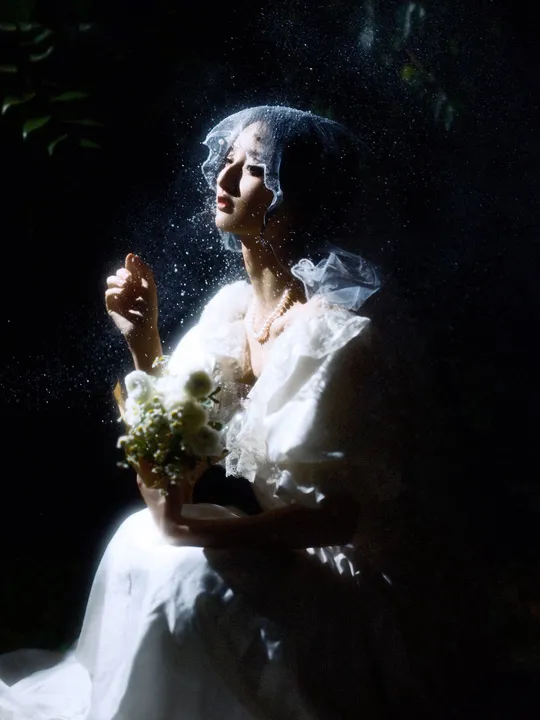 一位穿着婚纱的女人在点燃的窗户前拿着花