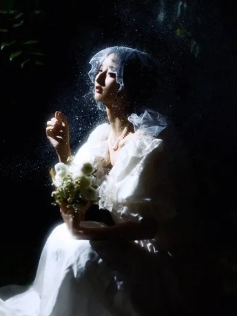 一位穿着婚纱的女人在点燃的窗户前拿着花