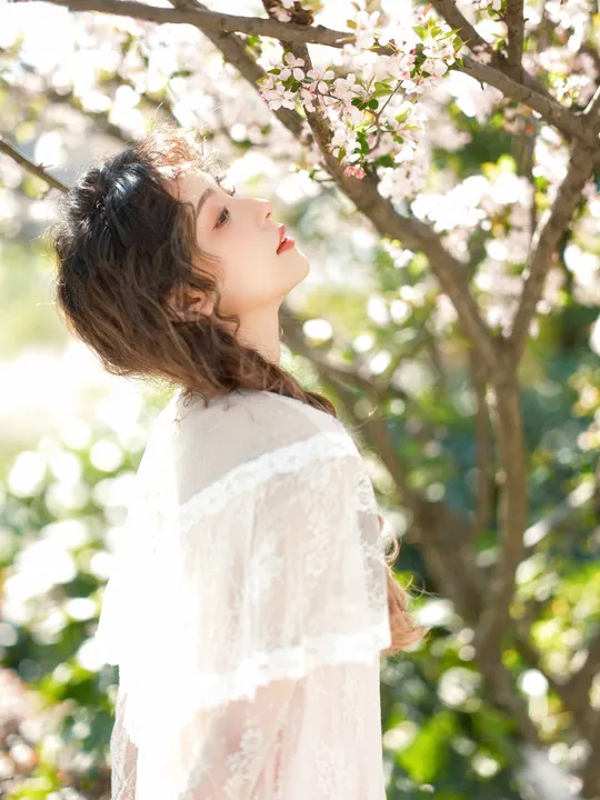 一位美丽的年轻女子穿着白色裙子站在一朵盛开的树下