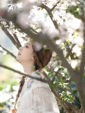 一位美丽的年轻女子站在一朵盛开的白色花树下面