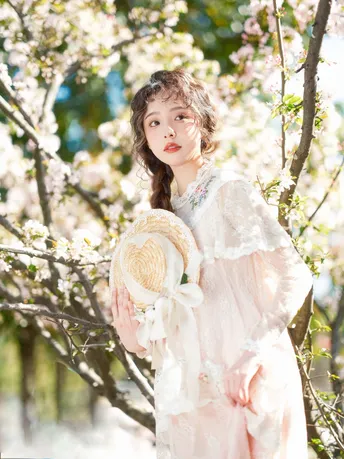 美丽年轻的女子穿着白色裙子 戴着帽子 站在盛开的花树下。