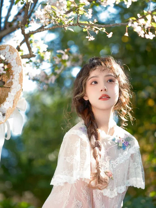 一个小女孩穿着白色裙子站在一朵盛开的树下