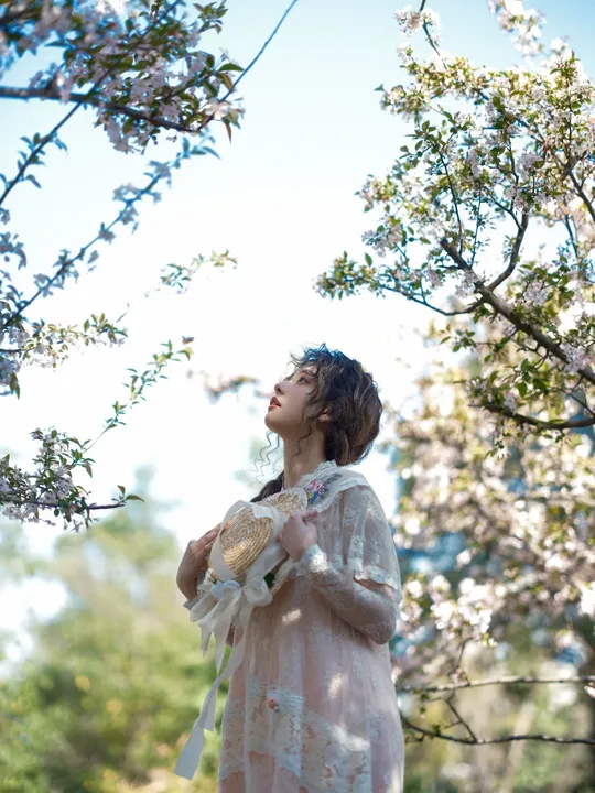 一个穿着白色连衣裙的年轻女子 手里拿着一朵粉色花 抬头望向天空。
