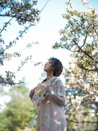 一个穿着白色连衣裙的年轻女子 手里拿着一朵粉色花 抬头望向天空。