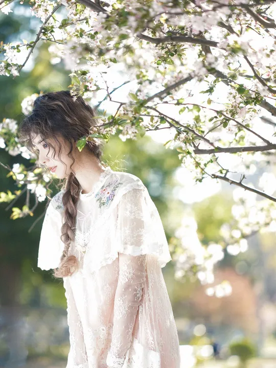 一位美丽的年轻女子穿着一件白色婚纱站在一朵盛开的树下 她的头发上插着鲜花。