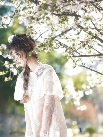 一位美丽的年轻女子穿着一件白色婚纱站在一朵盛开的树下 她的头发上插着鲜花。