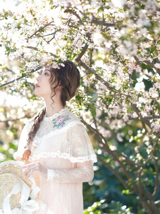 一位美丽的年轻女士穿着一件白色连衣裙站在樱花盛开的一棵树下