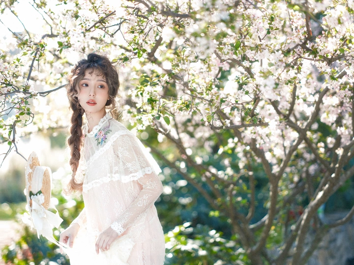 美丽的年轻女子穿着白色连衣裙站在一个开满树木和花朵的花园里