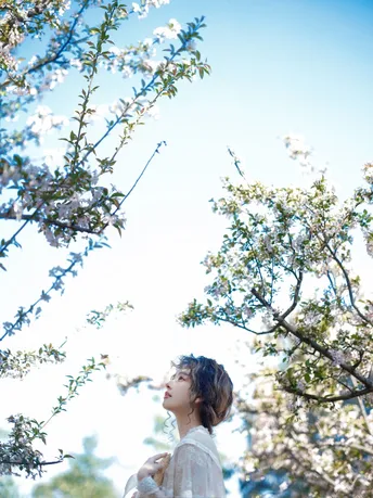 一位年轻女子站在一朵盛开的树下仰望天空